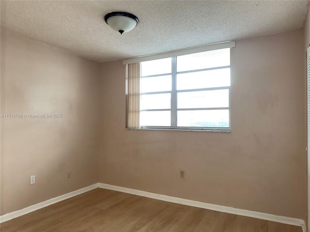 empty room with a textured ceiling, baseboards, and wood finished floors