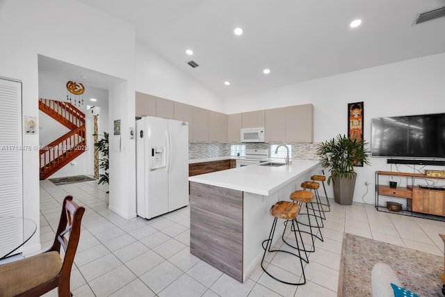 kitchen featuring white appliances, sink, gray cabinets, a kitchen bar, and kitchen peninsula