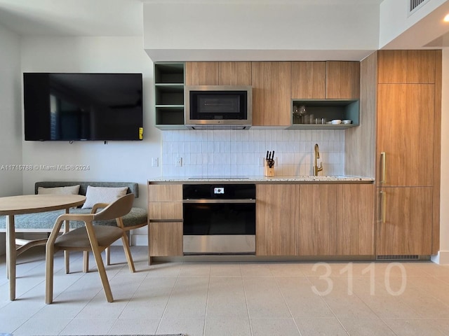 kitchen featuring decorative backsplash, light stone countertops, stainless steel appliances, and light tile patterned floors