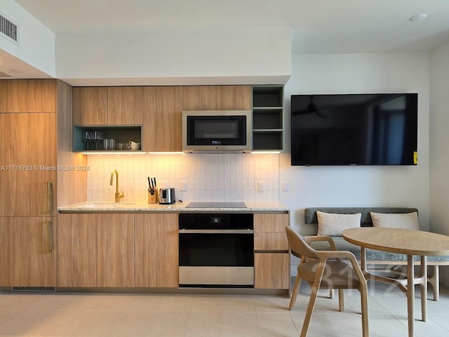 kitchen with sink, decorative backsplash, light tile patterned floors, light stone countertops, and appliances with stainless steel finishes