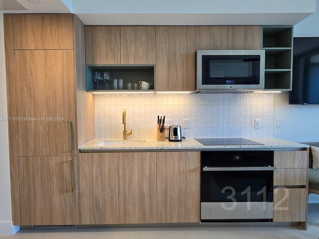 kitchen featuring light stone countertops, backsplash, oven, and sink