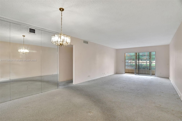 spare room with carpet flooring, a notable chandelier, and a textured ceiling