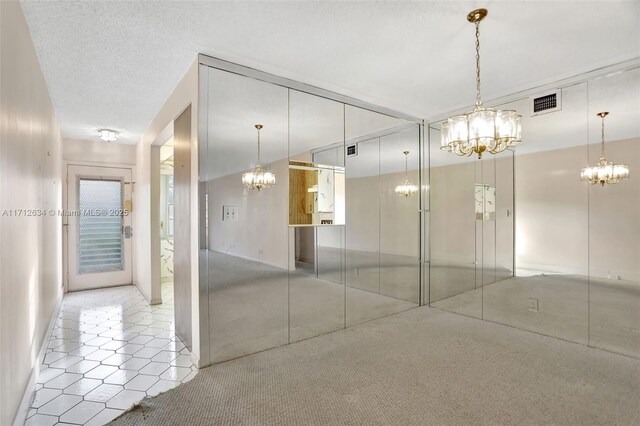 carpeted empty room featuring a textured ceiling and a notable chandelier