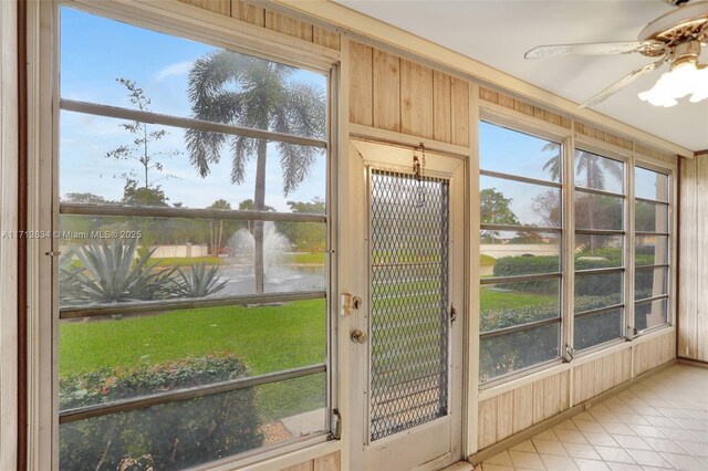 doorway to outside with wooden walls, ceiling fan, and light tile patterned floors