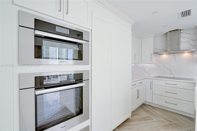 kitchen with white cabinetry, wall chimney exhaust hood, tasteful backsplash, double oven, and light parquet floors