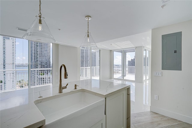 kitchen featuring electric panel, light stone counters, sink, and pendant lighting