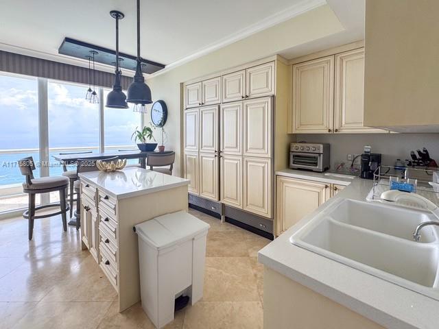 kitchen featuring pendant lighting, a center island, cream cabinets, crown molding, and sink