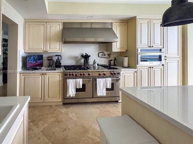 kitchen with cream cabinetry, appliances with stainless steel finishes, and wall chimney exhaust hood