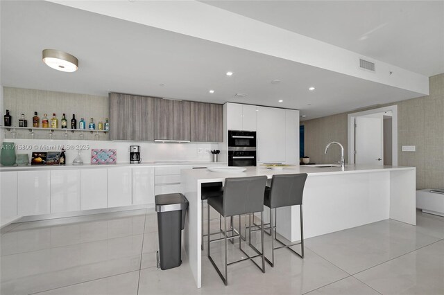 kitchen with white cabinetry, a kitchen breakfast bar, light tile patterned floors, and a large island with sink