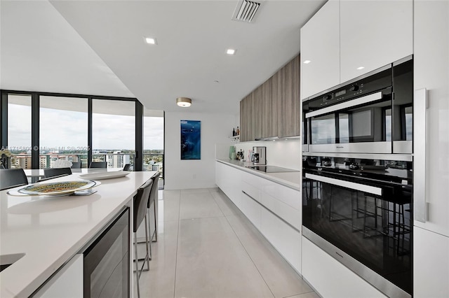 kitchen with white cabinetry, double oven, black electric stovetop, light tile patterned flooring, and beverage cooler