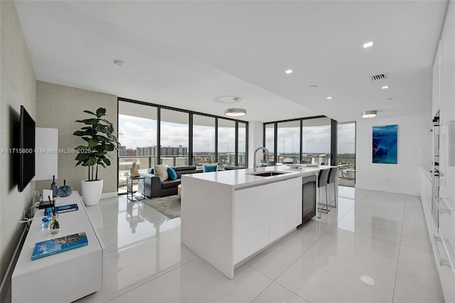 kitchen featuring a kitchen island with sink, sink, a wall of windows, and white cabinets