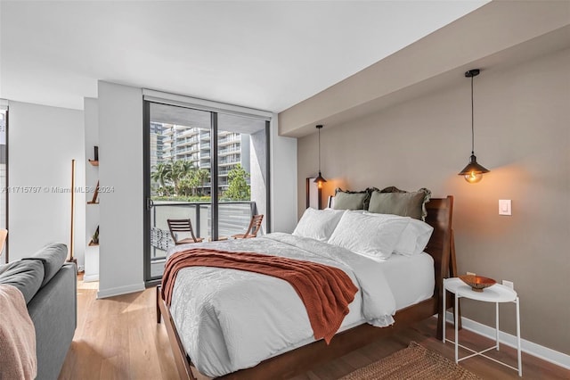 bedroom with access to exterior, wood-type flooring, and a wall of windows