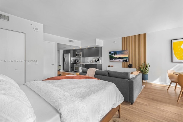 bedroom with light hardwood / wood-style flooring and stainless steel refrigerator with ice dispenser