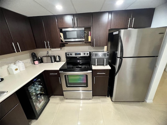 kitchen featuring dark brown cabinetry, a paneled ceiling, light tile patterned flooring, and appliances with stainless steel finishes