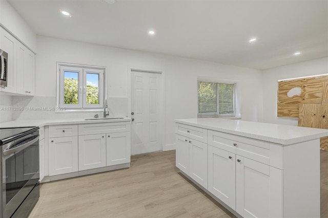 kitchen with light countertops, stainless steel electric range, light wood-style floors, white cabinets, and a sink