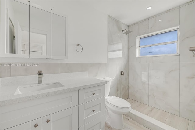 bathroom with a tile shower, vanity, toilet, and tile walls