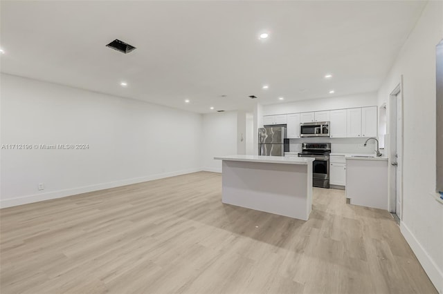 kitchen with sink, a kitchen island, appliances with stainless steel finishes, light hardwood / wood-style floors, and white cabinetry