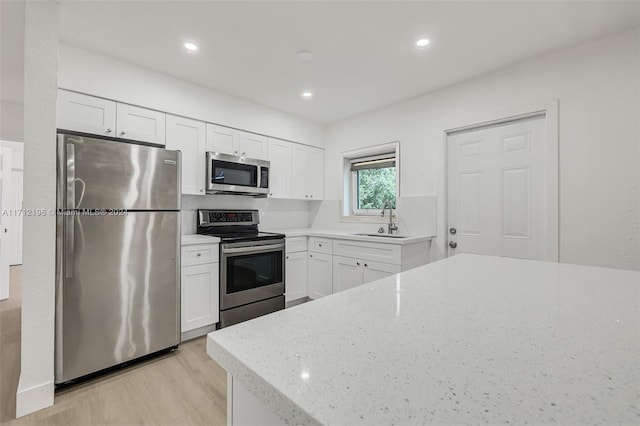 kitchen with light stone countertops, light wood-type flooring, stainless steel appliances, sink, and white cabinets