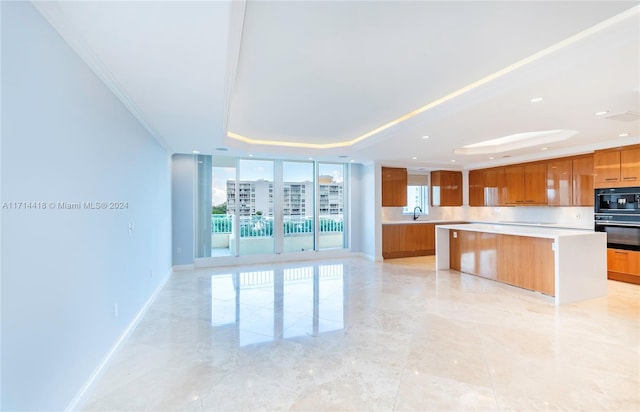 kitchen with oven, a center island, a raised ceiling, and ornamental molding