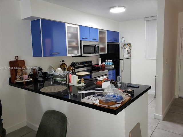 kitchen with light tile patterned flooring, appliances with stainless steel finishes, kitchen peninsula, and blue cabinets