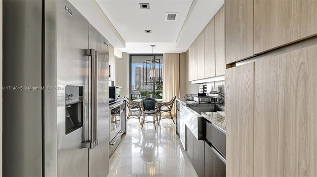 kitchen with pendant lighting, light brown cabinets, sink, stainless steel fridge, and light stone countertops