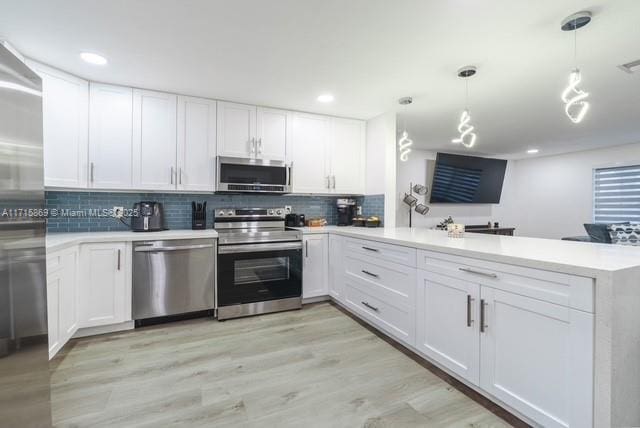 kitchen with stainless steel appliances, white cabinetry, kitchen peninsula, and decorative light fixtures