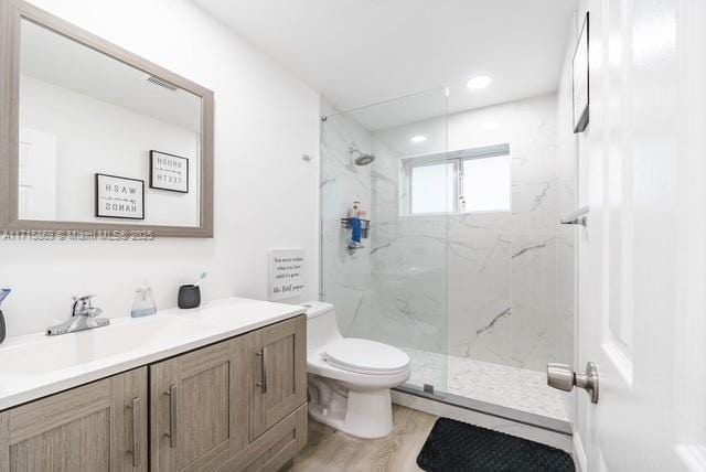 bathroom featuring vanity, hardwood / wood-style flooring, a shower with shower door, and toilet