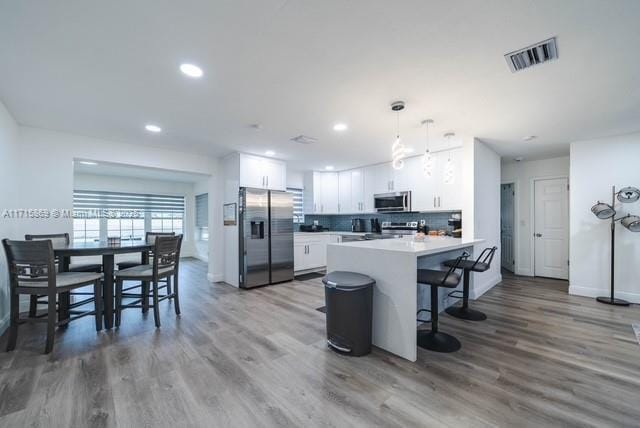 kitchen with wood-type flooring, appliances with stainless steel finishes, white cabinets, and decorative light fixtures