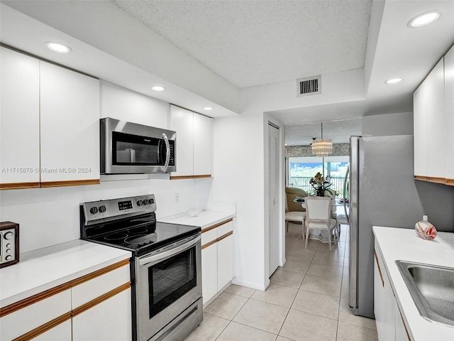 kitchen featuring pendant lighting, an inviting chandelier, light tile patterned floors, appliances with stainless steel finishes, and white cabinetry