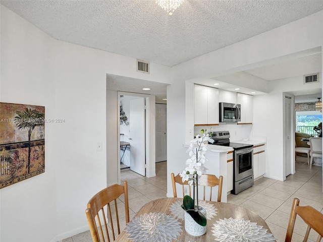 kitchen featuring white cabinets, light tile patterned floors, a textured ceiling, and stainless steel appliances