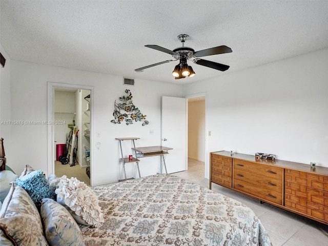 tiled bedroom featuring a textured ceiling, a walk in closet, a closet, and ceiling fan