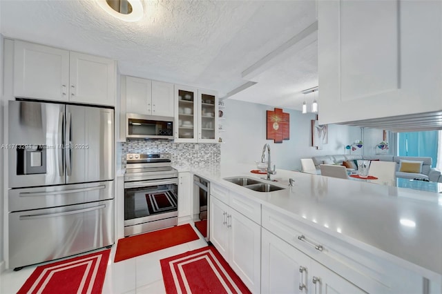 kitchen featuring white cabinets, glass insert cabinets, stainless steel appliances, light countertops, and a sink