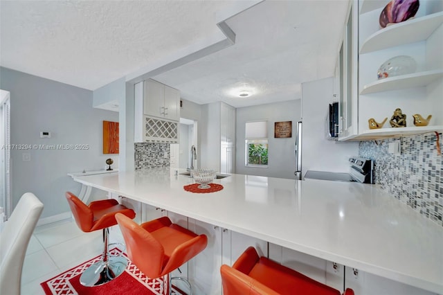 kitchen with kitchen peninsula, sink, white cabinets, electric stove, and a breakfast bar