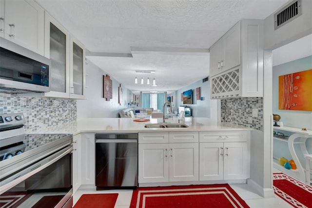 kitchen with a textured ceiling, white cabinets, stainless steel appliances, tasteful backsplash, and sink