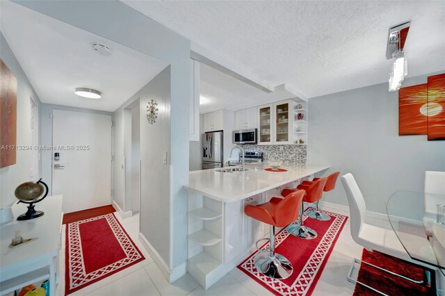 kitchen featuring a kitchen bar, appliances with stainless steel finishes, white cabinets, kitchen peninsula, and backsplash