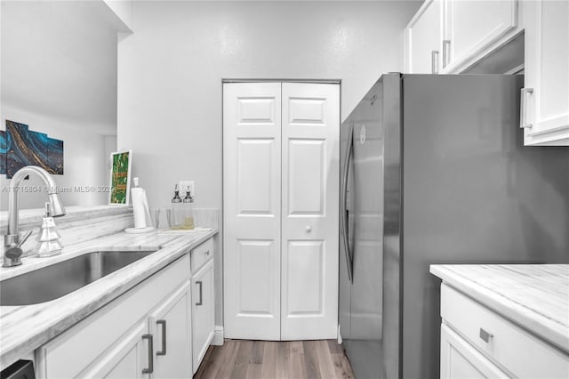 kitchen featuring white cabinets, sink, stainless steel fridge, light stone countertops, and wood-type flooring