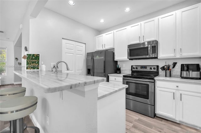 kitchen with stainless steel appliances, light stone counters, light hardwood / wood-style floors, a breakfast bar area, and white cabinets