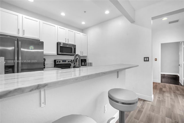 kitchen featuring beam ceiling, light stone countertops, white cabinetry, stainless steel appliances, and a kitchen bar