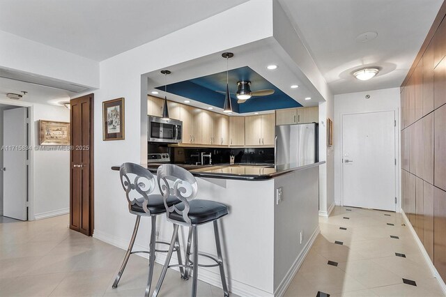 kitchen with ceiling fan, light brown cabinets, hanging light fixtures, a tray ceiling, and appliances with stainless steel finishes