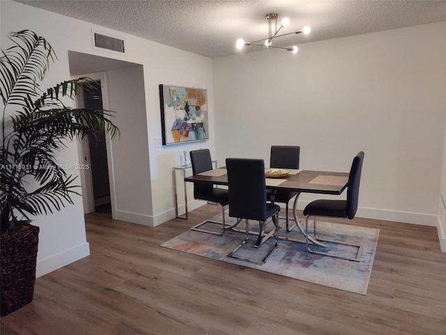 dining area with a textured ceiling, hardwood / wood-style flooring, and a notable chandelier