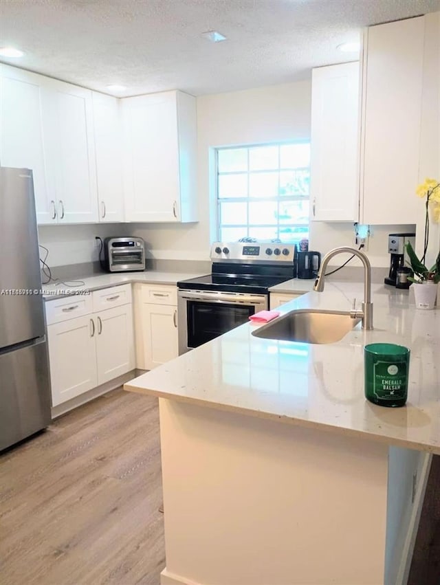 kitchen featuring sink, white cabinetry, a textured ceiling, appliances with stainless steel finishes, and light hardwood / wood-style floors