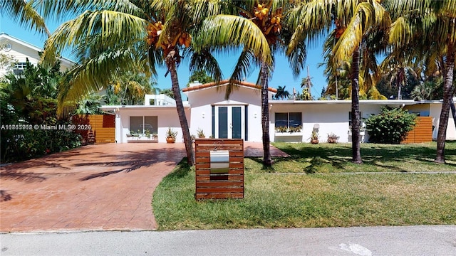 view of front of home with french doors, decorative driveway, a front lawn, and stucco siding