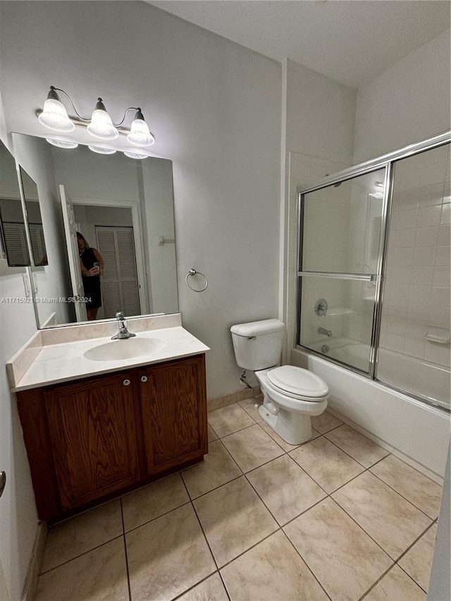 full bathroom with combined bath / shower with glass door, tile patterned floors, vanity, and toilet