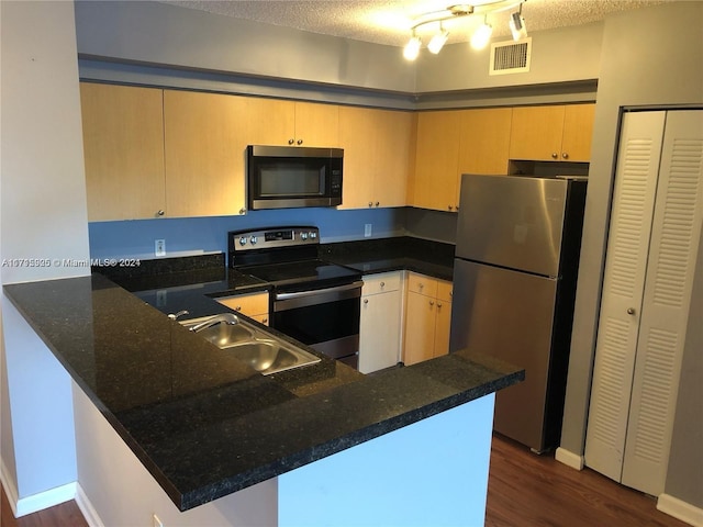 kitchen featuring kitchen peninsula, appliances with stainless steel finishes, dark stone counters, and sink