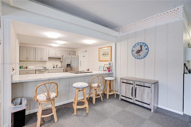 kitchen featuring dark colored carpet, a kitchen breakfast bar, kitchen peninsula, and stainless steel appliances