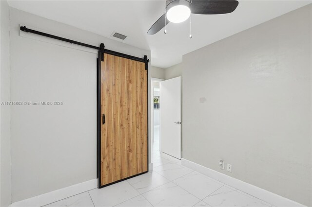 unfurnished bedroom featuring a barn door and ceiling fan