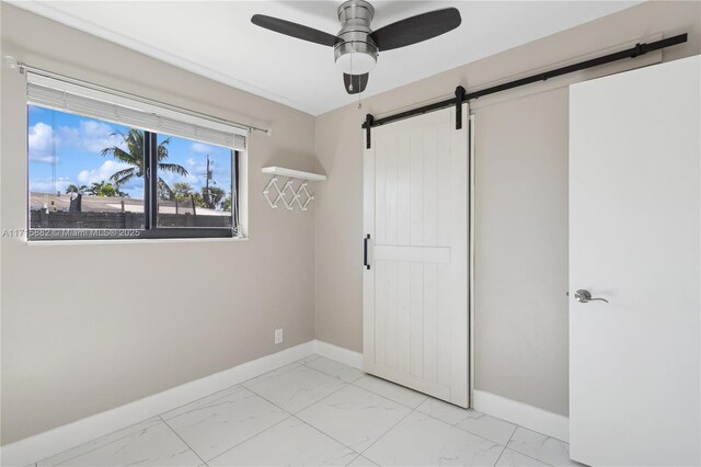 unfurnished bedroom featuring a barn door and ceiling fan