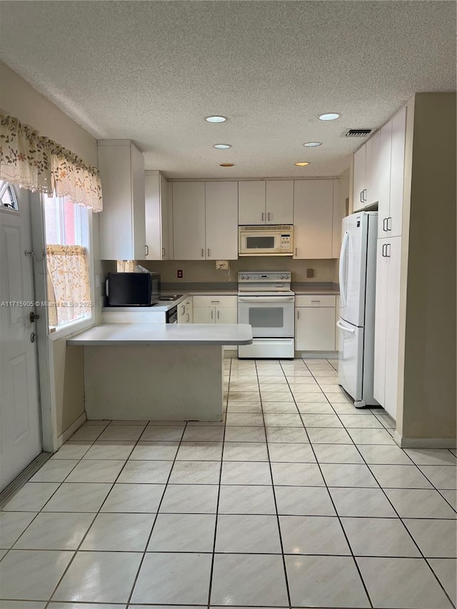 kitchen with a textured ceiling, kitchen peninsula, light tile patterned floors, and white appliances