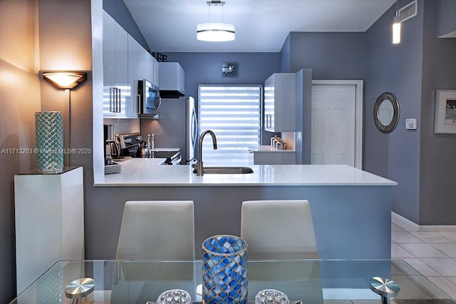 kitchen with pendant lighting, stainless steel appliances, light countertops, white cabinetry, and a sink