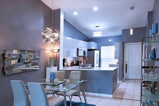 kitchen with stainless steel microwave, freestanding refrigerator, light countertops, white cabinetry, and pendant lighting